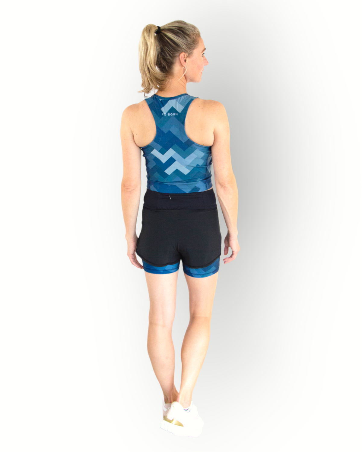 A woman wearing a black sports short with a camo blue print layer underneath. The short has an overlay fabric and an inner short, and there is a small pocket with zipper at the back inside the waistband.