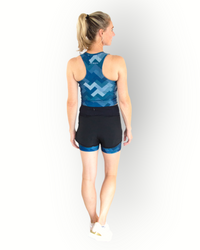 A woman wearing a black sports short with a camo blue print layer underneath. The short has an overlay fabric and an inner short, and there is a small pocket with zipper at the back inside the waistband.