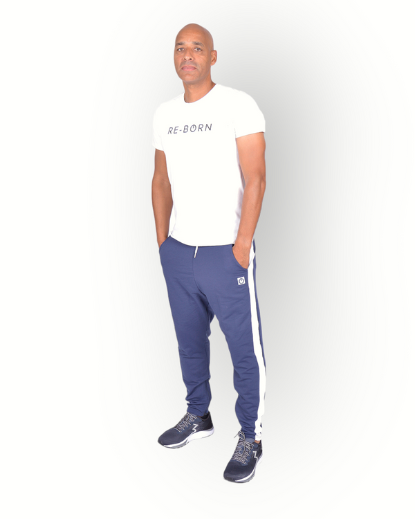 A man wearing navy blue and white side panel pants with zippers at legs and with a logo on the back of the leg, paired with a white RE-BORN logo T-shirt..