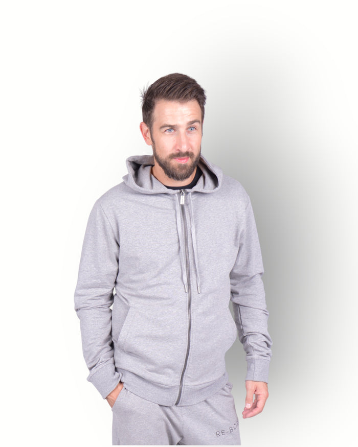 A man wearing a long sleeve full zip hooded top in grey, with side pockets and a scuba neck and printed E-BORN SPORTS on the back.