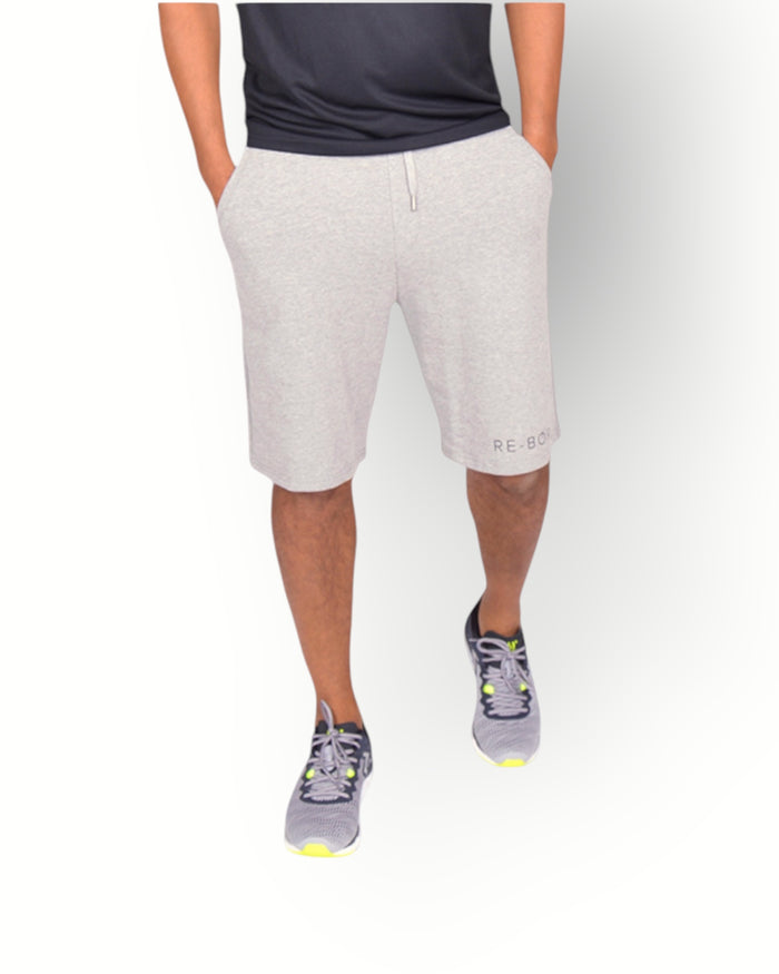 A man wearing a grey fleece short with a drawcord waistband and two side pockets, paired with a dark shirt and grey sneakers.
