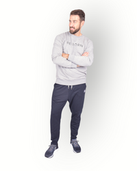 A male model wearing black poly side panel pants with white contrast with side pockets and zippers at the legs and combined with a grey sweater.