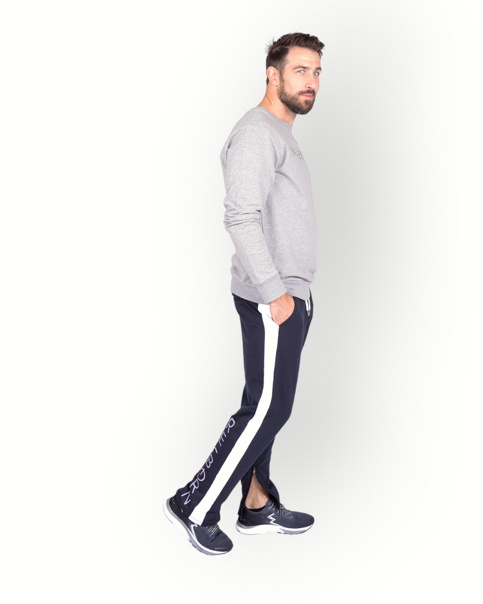 A male model wearing black poly side panel pants with white contrast with side pockets and zippers at the legs and combined with a grey sweater.