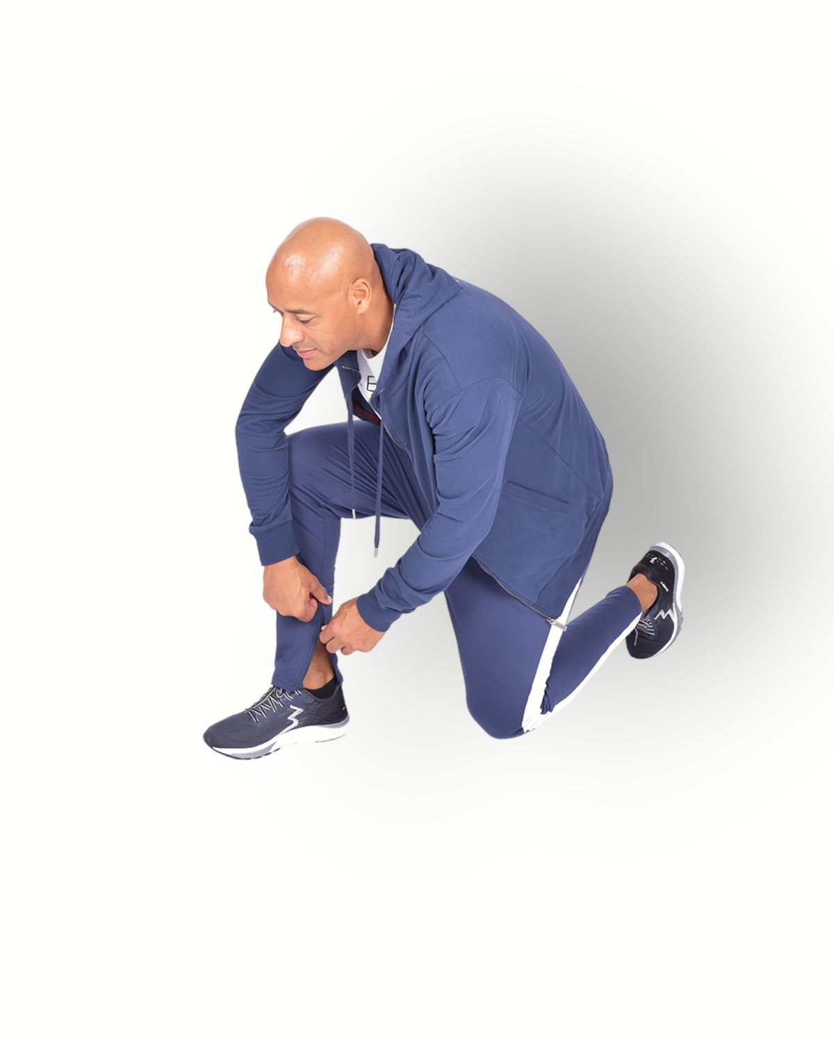 A man wearing navy blue and white side panel pants with zippers at legs and with a logo on the back of the leg, paired with a navy full zipped hooded jacket.