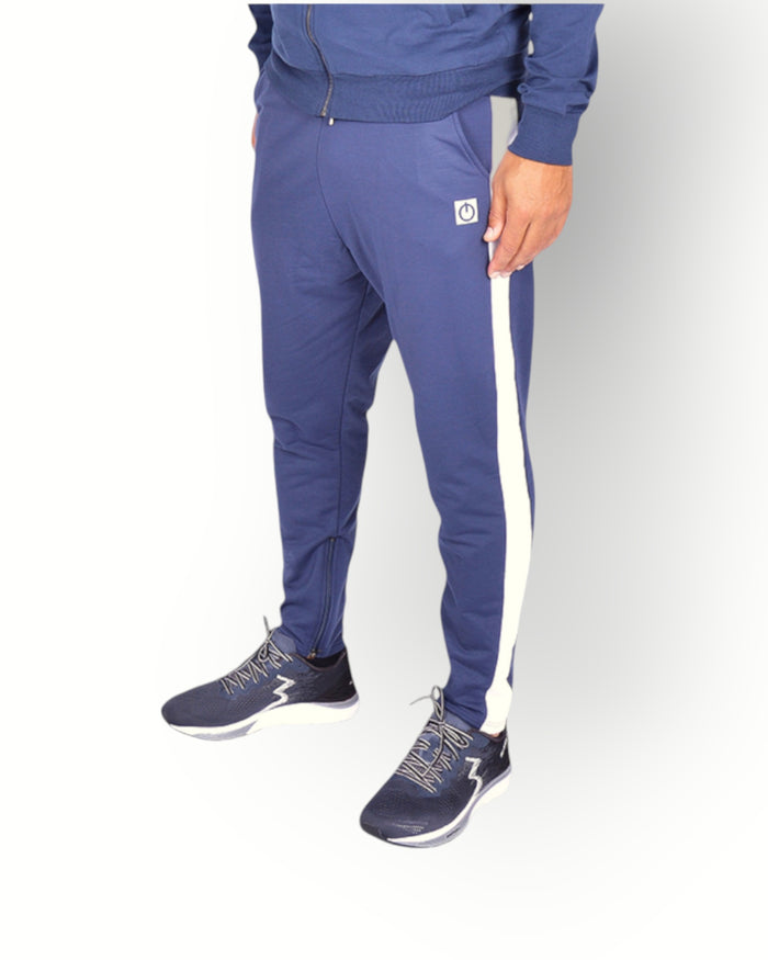 A man wearing navy blue and white side panel pants with a logo on the back of the leg, paired with a navy full zipped hooded jacket.