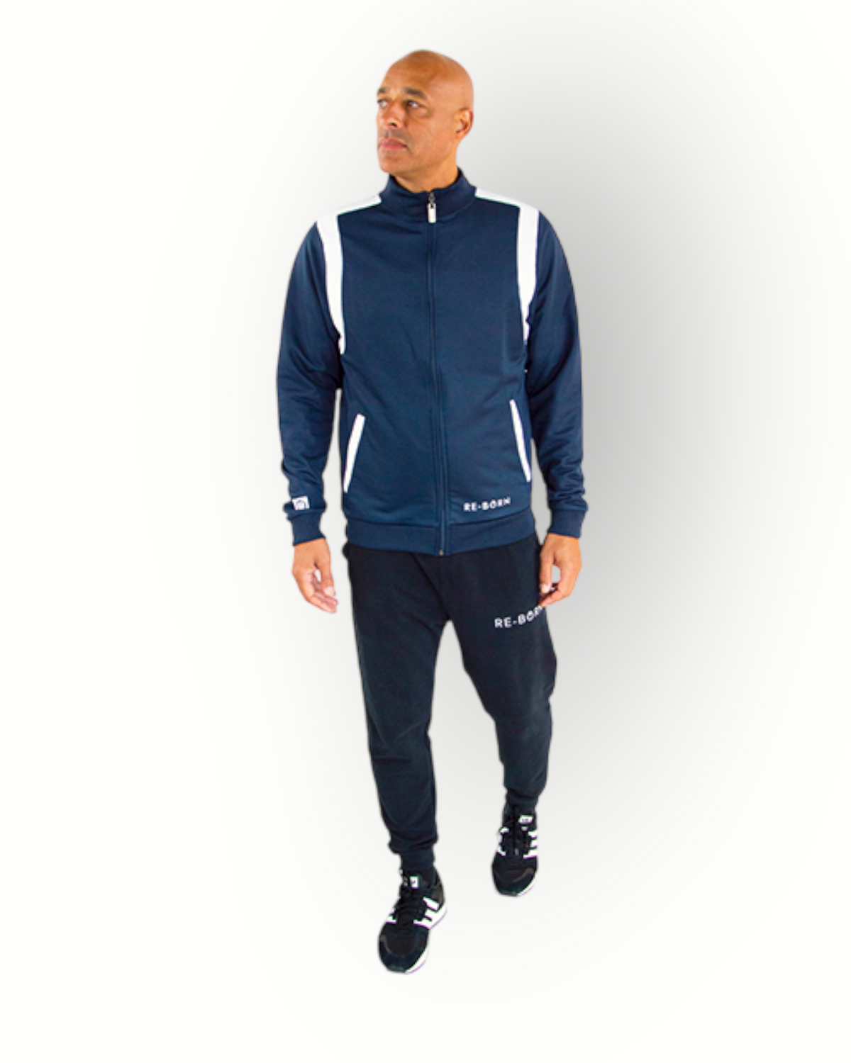 A man wearing a navy and white color block tracktop with a full zipper, high collar, and side pockets.