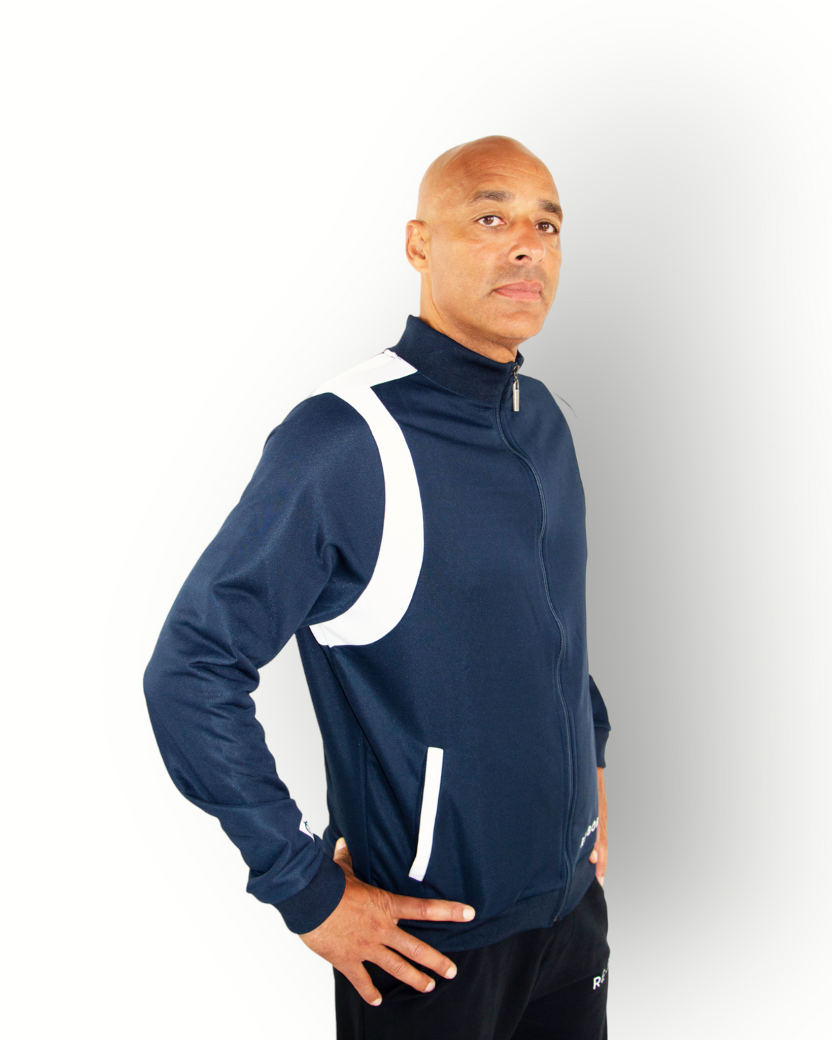 A man wearing a navy and white color block tracktop with a full zipper, high collar, and side pockets.