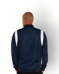 A man wearing a navy and white color block tracktop with a full zipper, high collar, and side pockets.