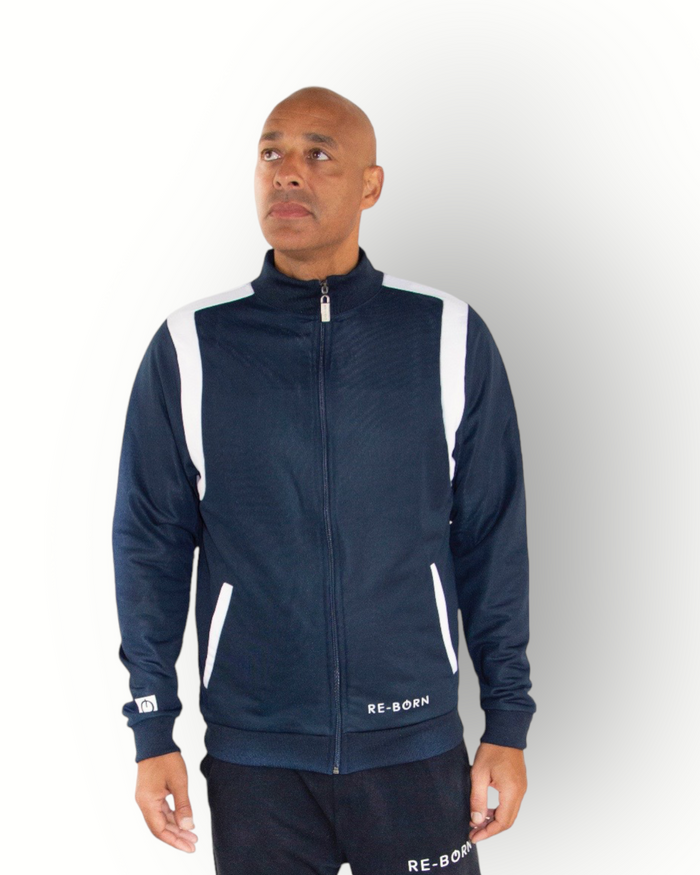 A man wearing a navy and white color block tracktop with a full zipper, high collar, and side pockets.