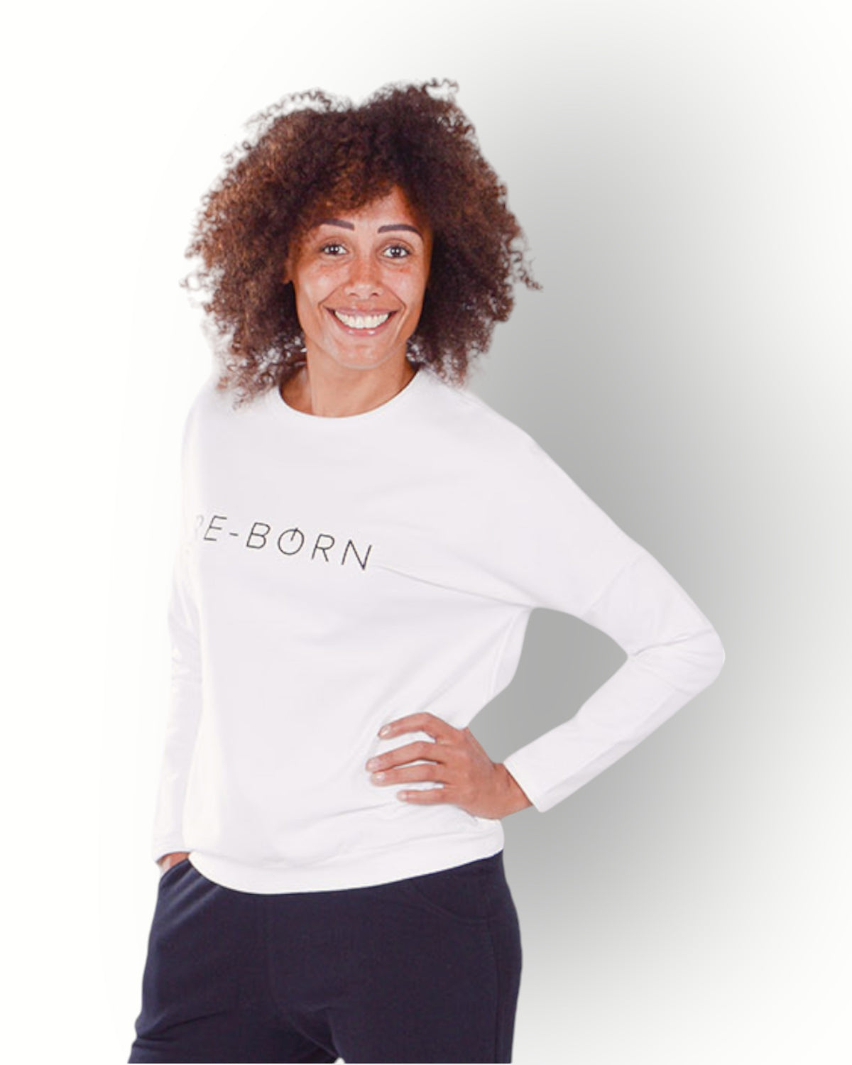 Woman wearing a white crew top with black RE-BORN logo printed on chest in super soft fabric.