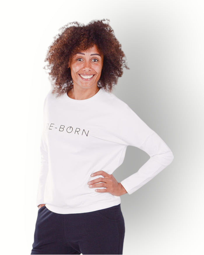 Woman wearing a white crew top with black RE-BORN logo printed on chest in super soft fabric.