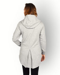 A woman facing away from the camera wearing a long sleeve grey full zip hoody with a hood and side pockets. and longer backside.