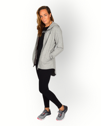 A woman wearing a long sleeve grey full zip hoody with a hood and side pockets. and longer backside.
