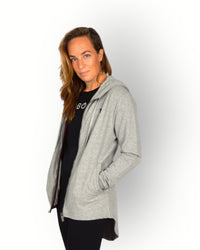 A woman wearing a long sleeve grey full zip hoody with a hood and side pockets. and longer backside.