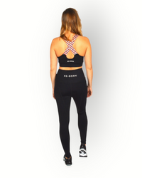 A woman standing and posing in a black sports bra with a cross-over elastic back, overlaid with a striped pattern on the elastic.