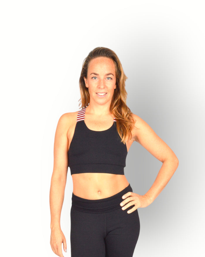 A woman standing and posing in a black sports bra with a cross-over elastic back, overlaid with a striped pattern on the elastic.