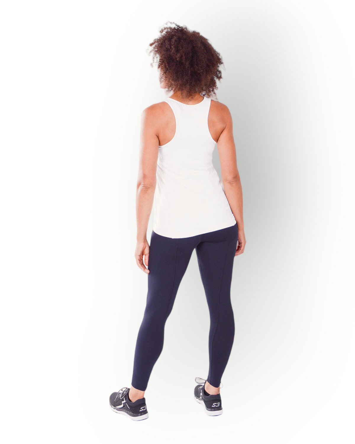 A woman wearing a white tank top with racerback standing against a white background.