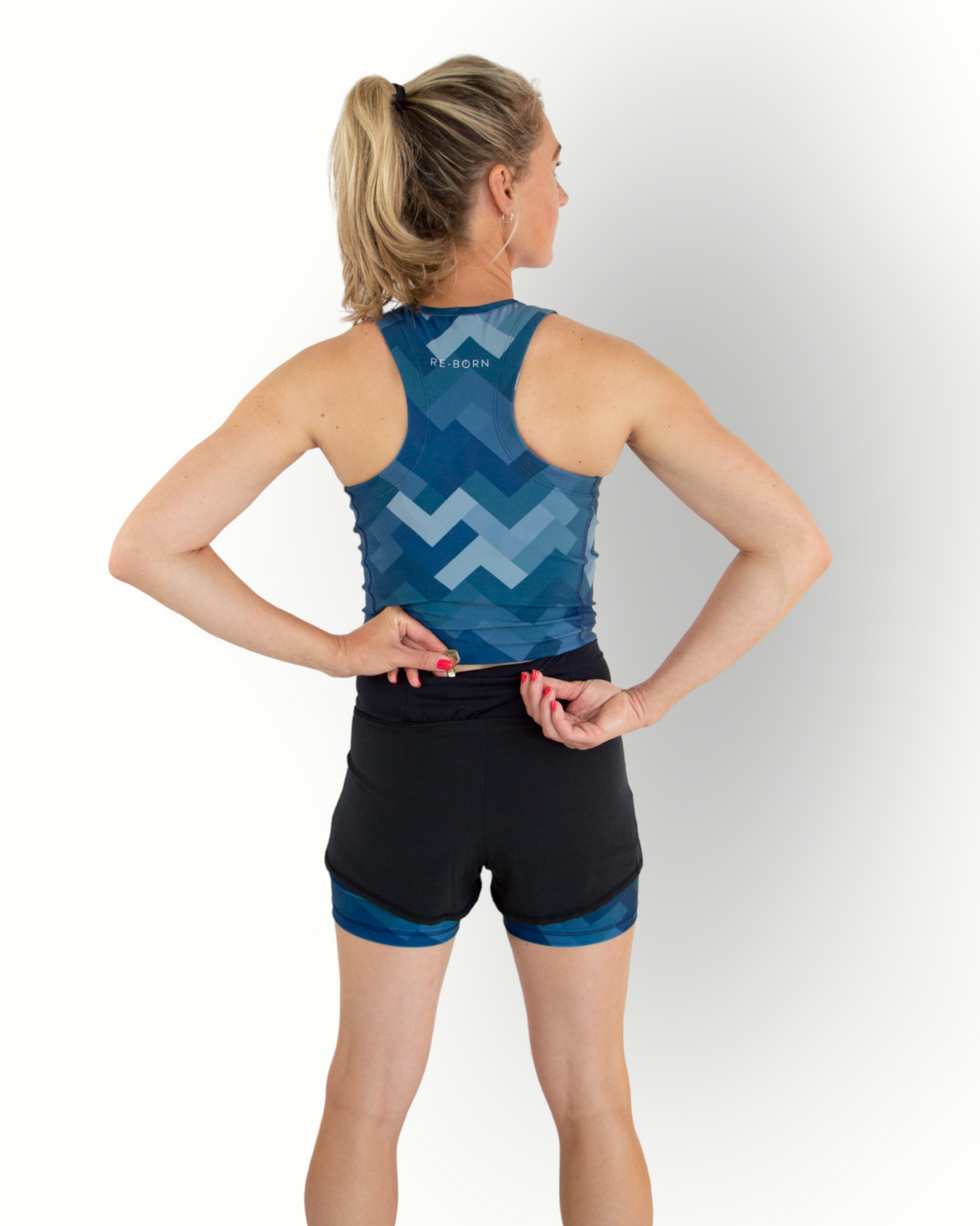 A woman wearing a black sports short with a camo blue print layer underneath. The short has an overlay fabric and an inner short, and there is a small pocket with zipper at the back inside the waistband.