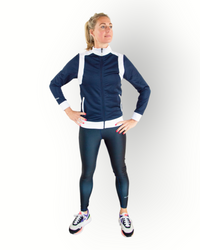 A woman wearing a navy and white color block training jacket with a full zipper and side pockets combined with the reversible sports legging.